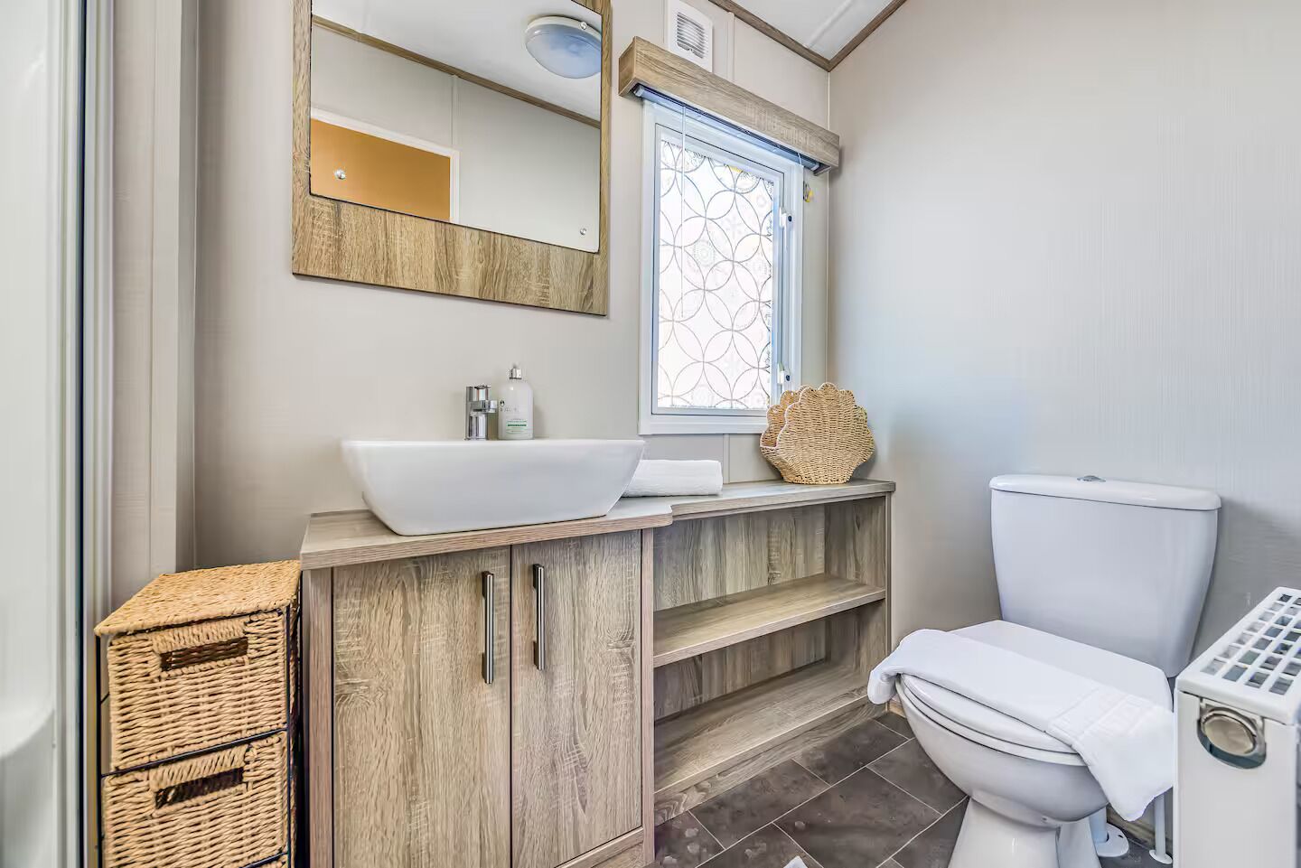 A bathroom with a wooden vanity, a white sink, a toilet, and a window with a decorative glass pattern.