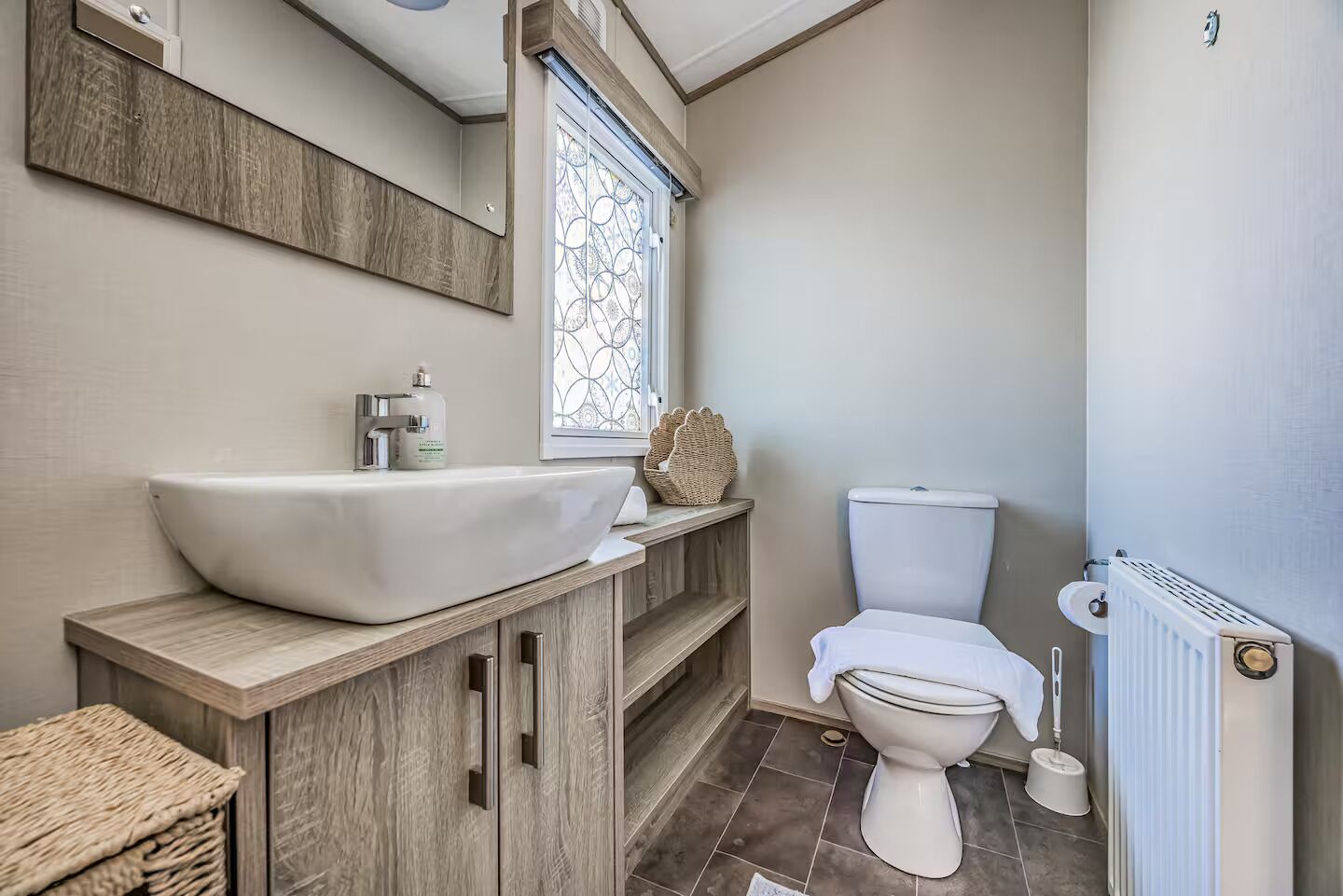 A bathroom with a vessel sink, a toilet, a window with a decorative pattern, and a radiator.