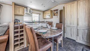 A compact kitchen with a dining area, wooden cabinets, and a built-in stove. - Lovely Lakeside Holiday Park Home  - Pass the Keys (Chichester)