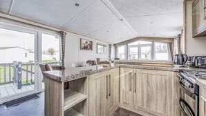 A modern kitchen with a large island, wooden cabinets, and a view of the outside. - Lovely Lakeside Holiday Park Home  - Pass the Keys (Chichester)