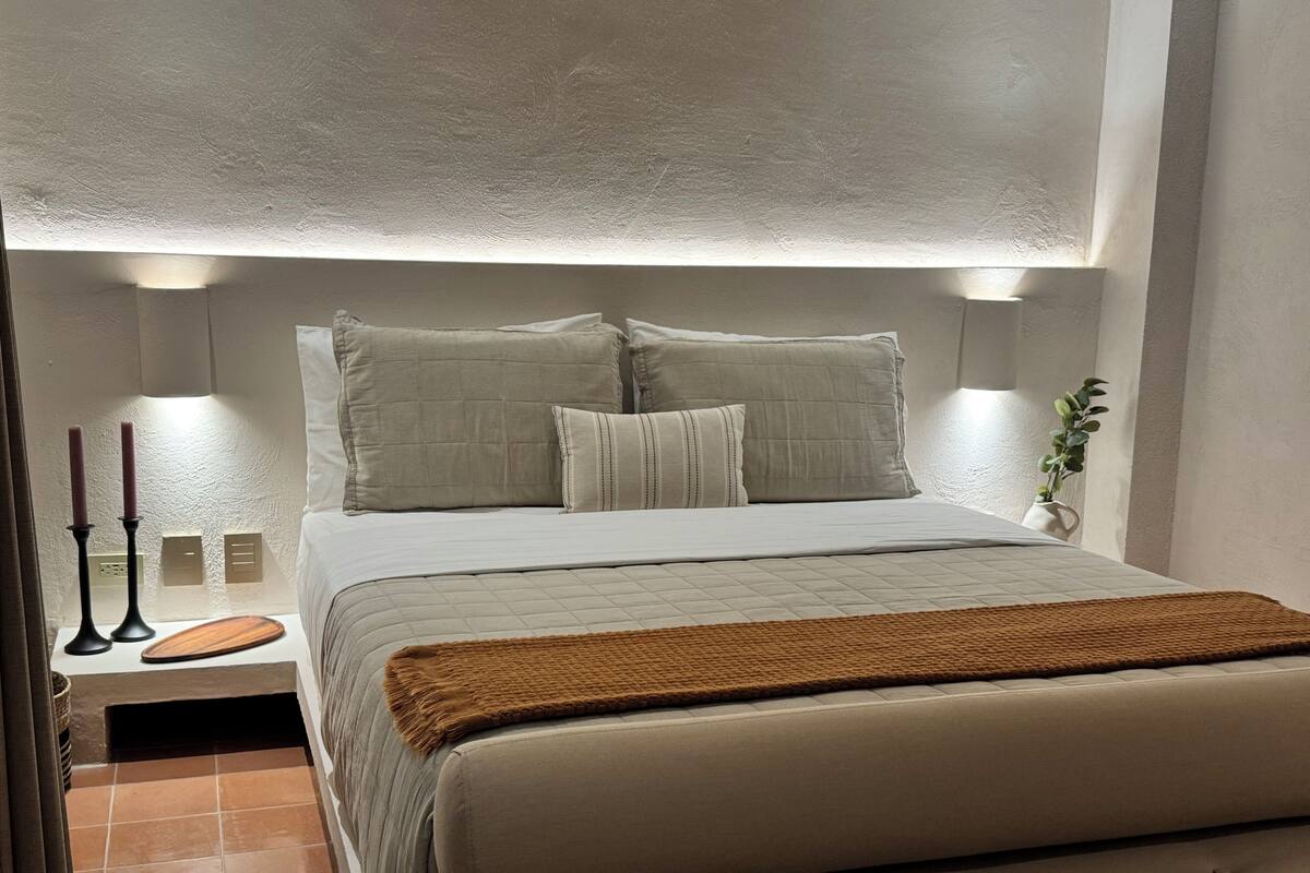 Une chambre à coucher avec un lit, des oreillers, une table de chevet et des lampes fixées au mur.