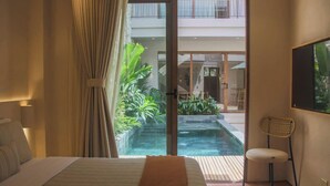 A bedroom with a bed, a chair, a sliding glass door leading to a pool area with plants.