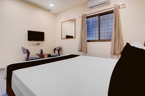 A hotel room with a bed, a television mounted on the wall, a small table with a chair, and a window with curtains. - Townhouse Oak Phaltan Shivjal City (Phaltan)