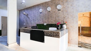 Una recepción con relojes mostrando diferentes zonas horarias, una pared verde y un diseño moderno.