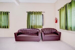 A room with two leather sofas, a fire extinguisher on the wall, and green curtains. - Townhouse Oak Phaltan Shivjal City (Phaltan)