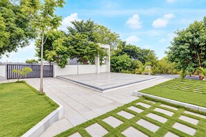 Un vaste espace extérieur doté d’une terrasse dallée, entouré de pelouse et d’arbres bien entretenus.