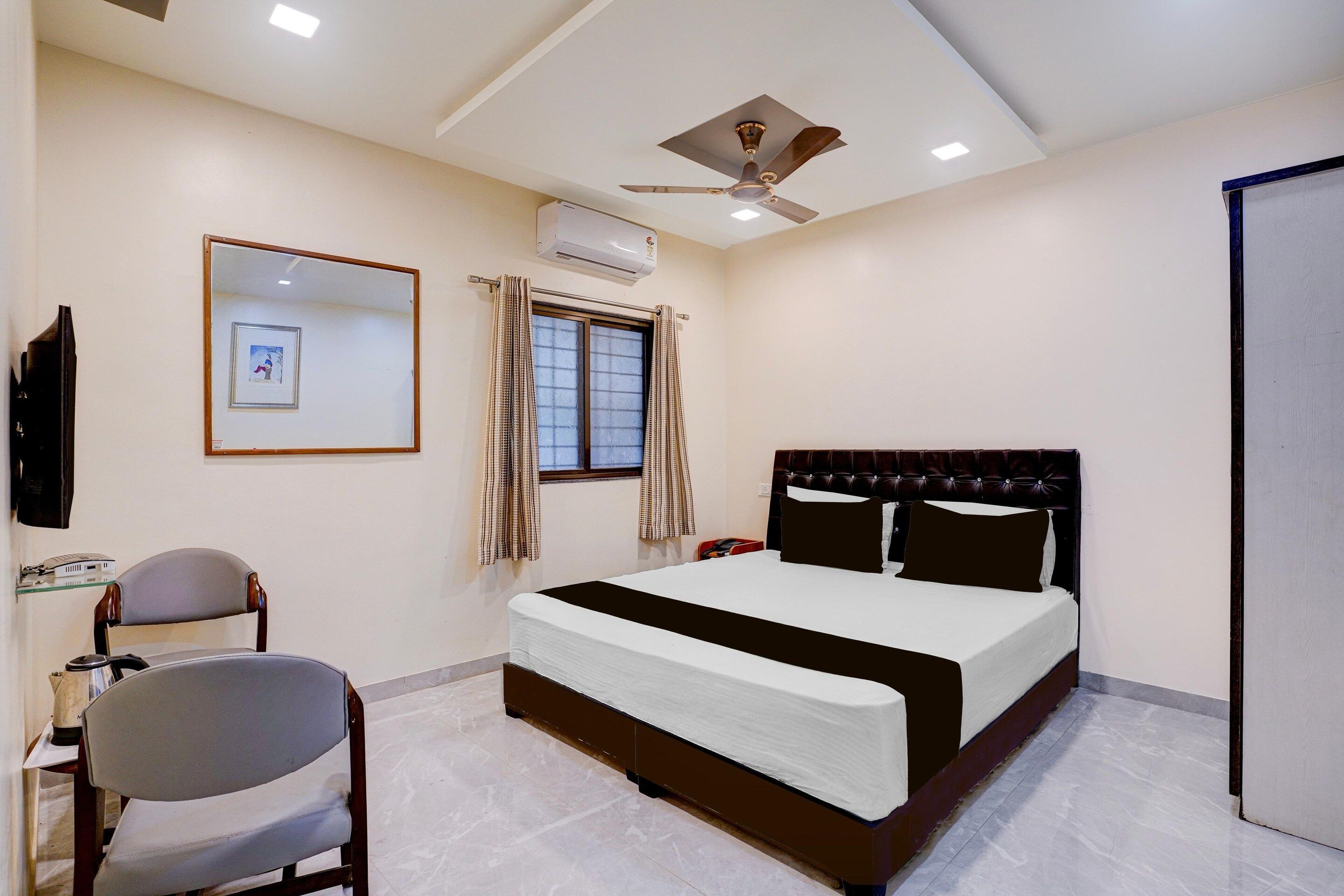 A hotel room with a bed, a chair, a desk, a ceiling fan, and an air conditioning unit.