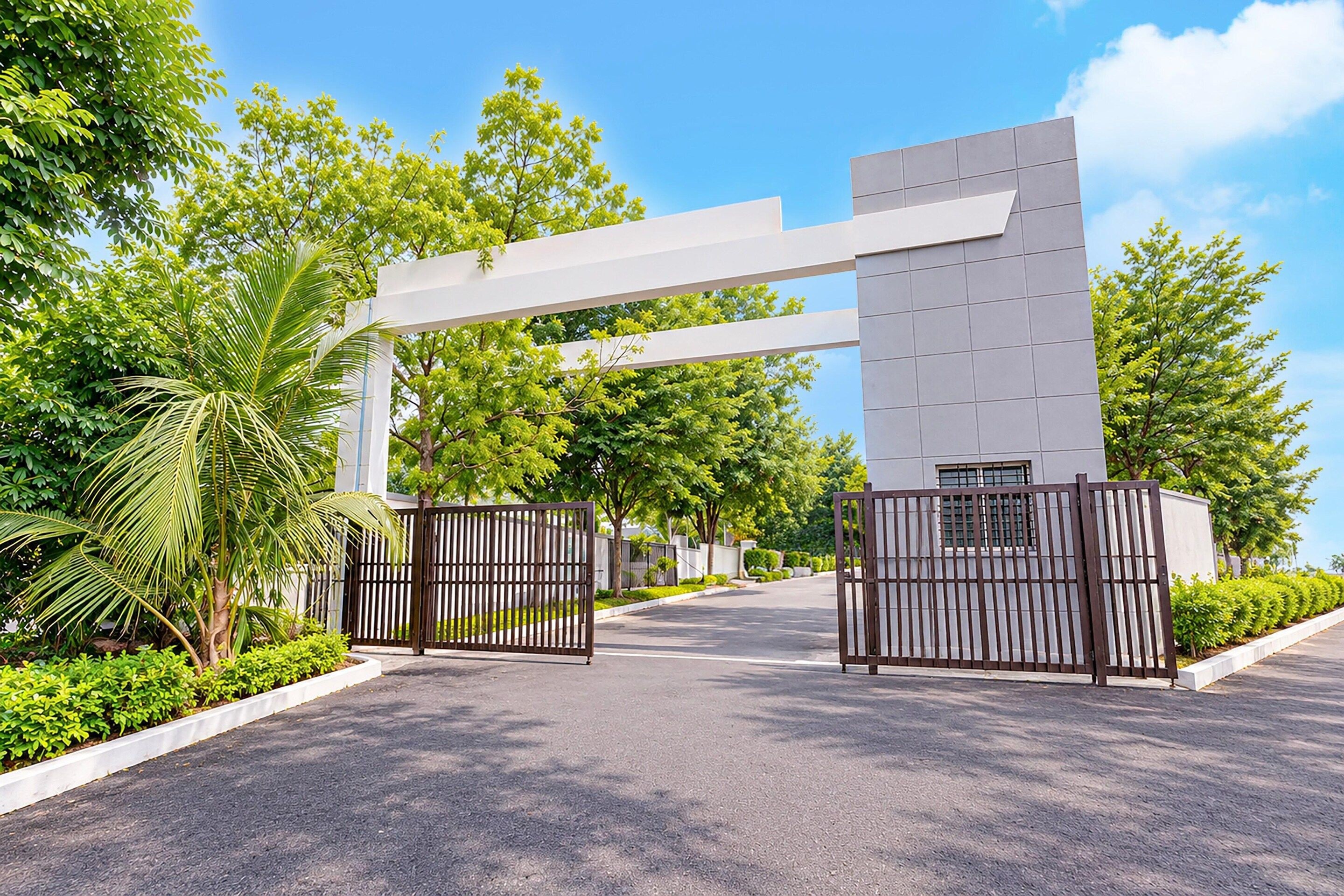 A gated entrance with a modern archway, surrounded by lush greenery and a clear sky.