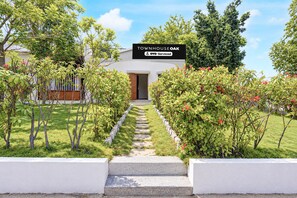 A residential property with a stone pathway leading to the entrance, surrounded by lush greenery and flowering plants. - Townhouse Oak Phaltan Shivjal City (Phaltan)