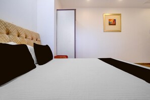 A hotel room with a large bed, a door, and a framed picture on the wall. - Townhouse Oak Phaltan Shivjal City (Phaltan)