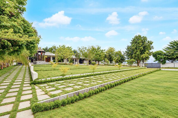 A landscaped garden with a paved walkway, neatly trimmed grass, and a variety of trees. - Townhouse Oak Phaltan Shivjal City (Phaltan)