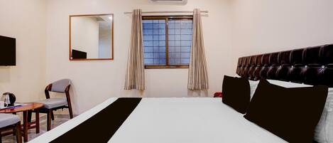 A hotel room with a bed, a chair, a desk, a mirror, and a window with curtains.