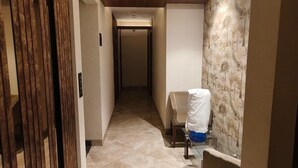 Un pasillo estrecho con una puerta de madera a la izquierda, suelo de baldosas y un papel tapiz estampado a la derecha.