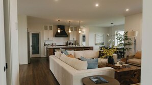 A modern kitchen with white cabinets, a central island, pendant lighting, and a dining area with a table and chairs.