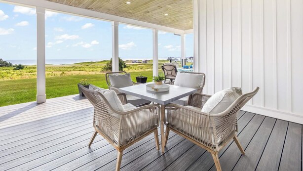 A covered outdoor seating area with a table and wicker chairs, overlooking a grassy landscape.