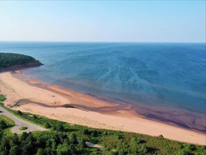 Eine Luftaufnahme einer Küstenlandschaft mit Sandstrand, klarem Wasser und einer kurvenreichen Straße, die durch ein bewaldetes Gebiet führt.