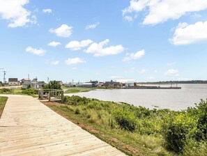 Ein hölzerner Steg führt zu einer Uferpromenade, im Hintergrund sind Gebäude zu sehen.
