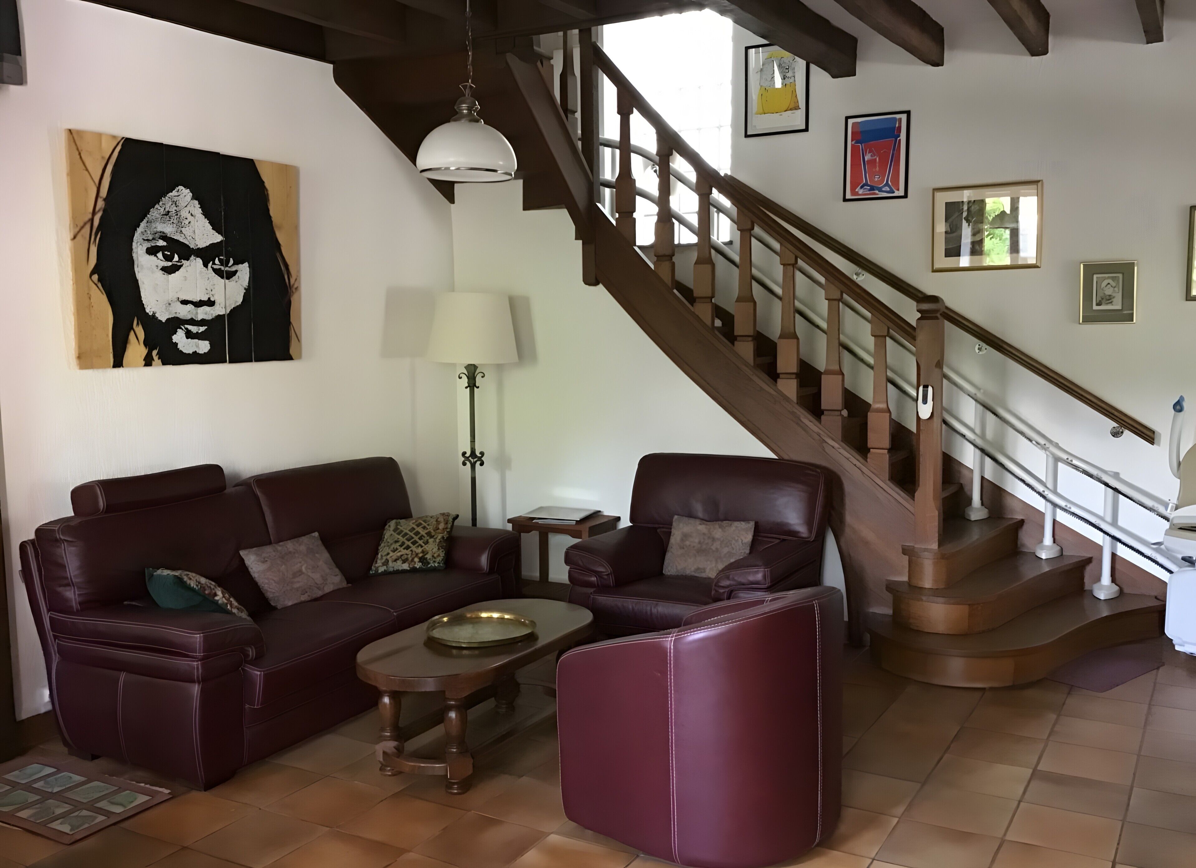 Een woonkamer met een bruine leren bank, een bijpassende fauteuil, een houten salontafel en een trap met houten leuningen.