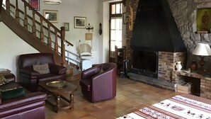 A living room with a fireplace, leather sofas, a wooden coffee table, and a staircase. - Holiday Home "Gîte for 6 People" with Private Terrace and Wi-Fi (La Chapelle)