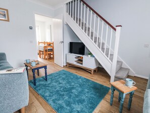 Ein Wohnzimmer mit Treppe, Fernseher, Essbereich und einem blauen Teppich.