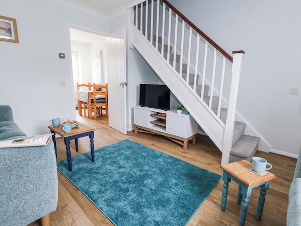 A living room with a staircase, a television, a dining area, and a blue rug. - Dolphin Cottage (Weymouth)