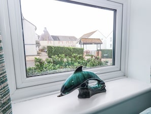 A window with a view of a residential area, a hedge, and a building with a pointed roof. - Dolphin Cottage (Weymouth)