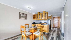 A modern kitchen with wooden cabinets, a dining area with a glass table and chairs, and a hallway with a wooden floor. - Pacific Terrace - Vista al mar- 4 huéspedes - Wifi (Viña del Mar)