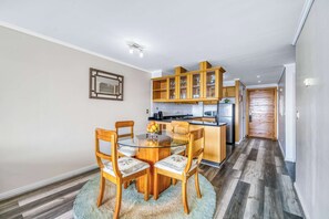 A modern kitchen with wooden cabinets, a dining area with a glass table and chairs, and a hallway with a wooden floor. - Pacific Terrace - Vista al mar- 4 huéspedes - Wifi (Viña del Mar)