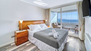 A hotel room with a bed, a nightstand, a lamp, a view of the sea, and a balcony with a table and chairs. - Pacific Terrace - Vista al mar- 4 huéspedes - Wifi (Viña del Mar)
