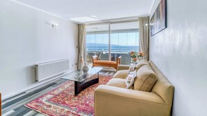 A modern living room with a sofa, a glass coffee table, a radiator, and a view of the outdoors. - Pacific Terrace - Vista al mar- 4 huéspedes - Wifi (Viña del Mar)