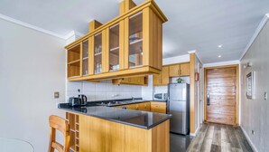 A kitchen with wooden cabinets, a black countertop, a refrigerator, and a microwave. - Pacific Terrace - Vista al mar- 4 huéspedes - Wifi (Viña del Mar)