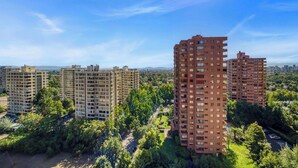 A high-rise residential building complex with multiple floors, surrounded by greenery and other buildings.