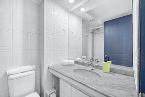 Um banheiro com paredes de azulejos brancos, pia de mármore, porta azul e um espelho.