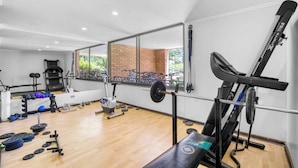 A gym with exercise equipment, a bench, and a mirror reflecting the outside.