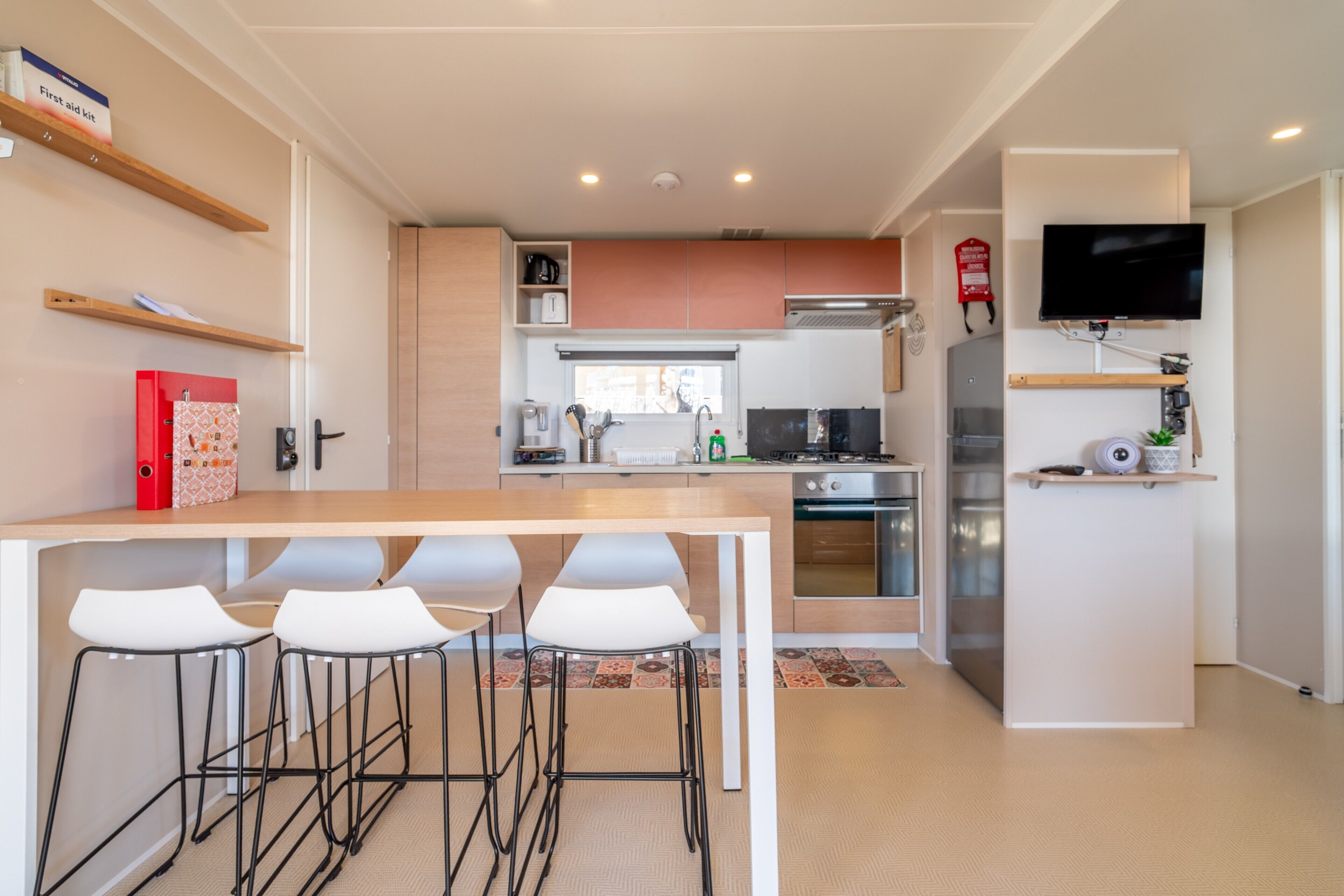 Una cucina moderna con isola centrale, sgabelli da bar, televisore a parete e estintore.