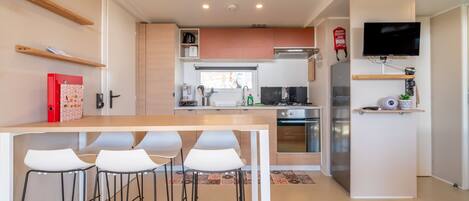Una cucina moderna con isola centrale, sgabelli da bar, televisore a parete e estintore.