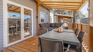 Une terrasse couverte avec une table et des chaises, un coin salon avec un banc, et une porte-fenêtre coulissante donnant sur un patio extérieur.