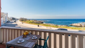 Ein Balkon mit Tisch für zwei Personen, mit Blick auf eine Küstenstraße und das Meer.