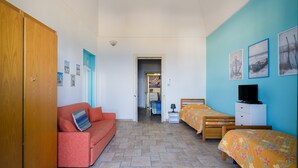 Ein Schlafzimmer mit einem Holzschrank, einem roten Sofa, zwei Einzelbetten, einem Fernseher und Kunstwerken an der Wand.