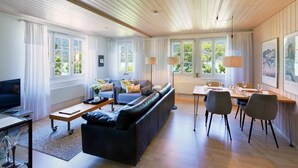 Uma sala de estar moderna com um sofá, uma mesa de centro, uma TV e uma área de jantar com cadeiras e uma mesa.