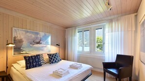 Un dormitorio con cama, una silla, un cuadro y una ventana con cortinas.