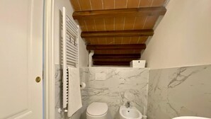 Une salle de bain comprenant des toilettes, un bidet et un lavabo, avec des murs en marbre et un plafond en bois.