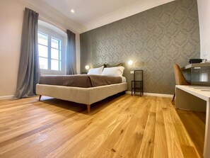 A bedroom with a bed, a desk, a chair, a window with curtains, and a patterned wall. - Residenza d'epoca dei Fondachi (Sarzana)