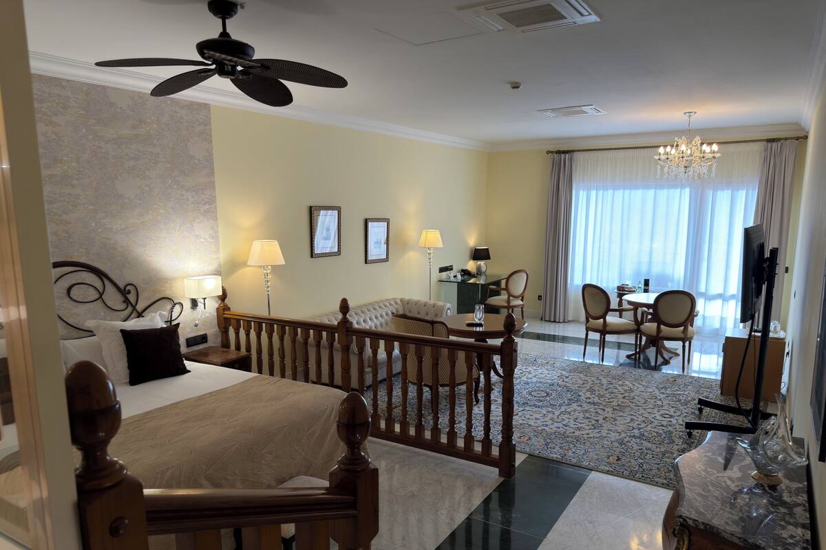 A hotel room with a bed, a desk, a dining area, and a living area.