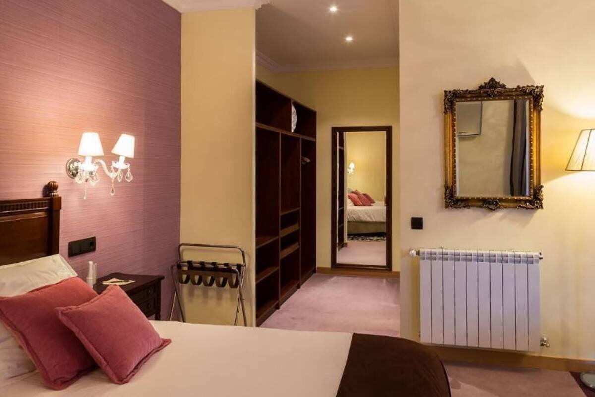 A hotel room with a bed, a nightstand, a lamp, a wardrobe, a mirror, and a radiator.