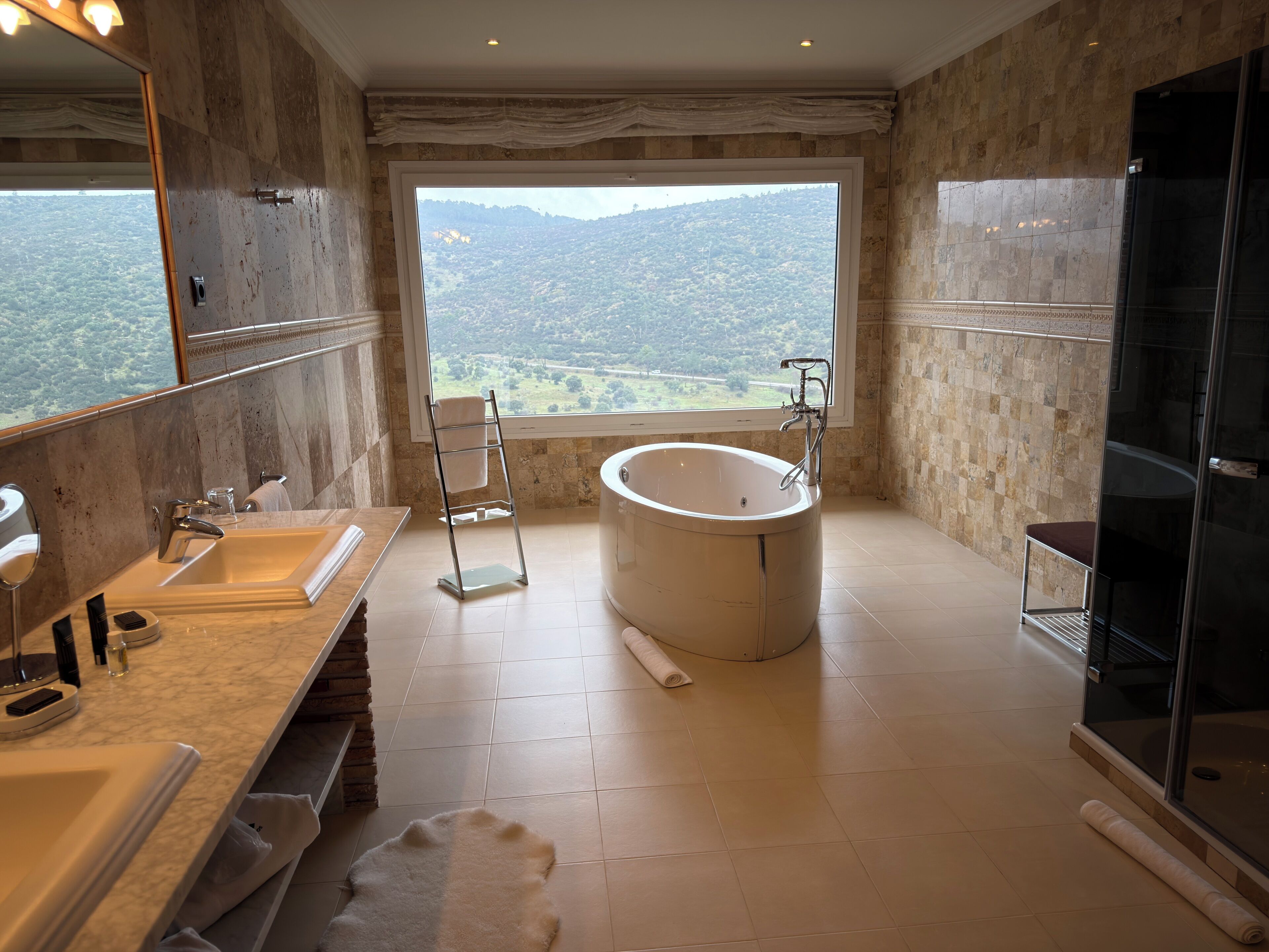 Un baño con una bañera grande, un tocador con espejo, un perchero y vistas a un paisaje montañoso.
