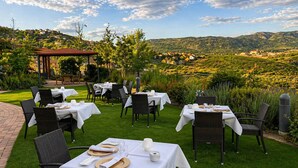Un área de comedor al aire libre con mesas dispuestas para los comensales, rodeada de exuberante vegetación y una vista panorámica de colinas ondulantes.
