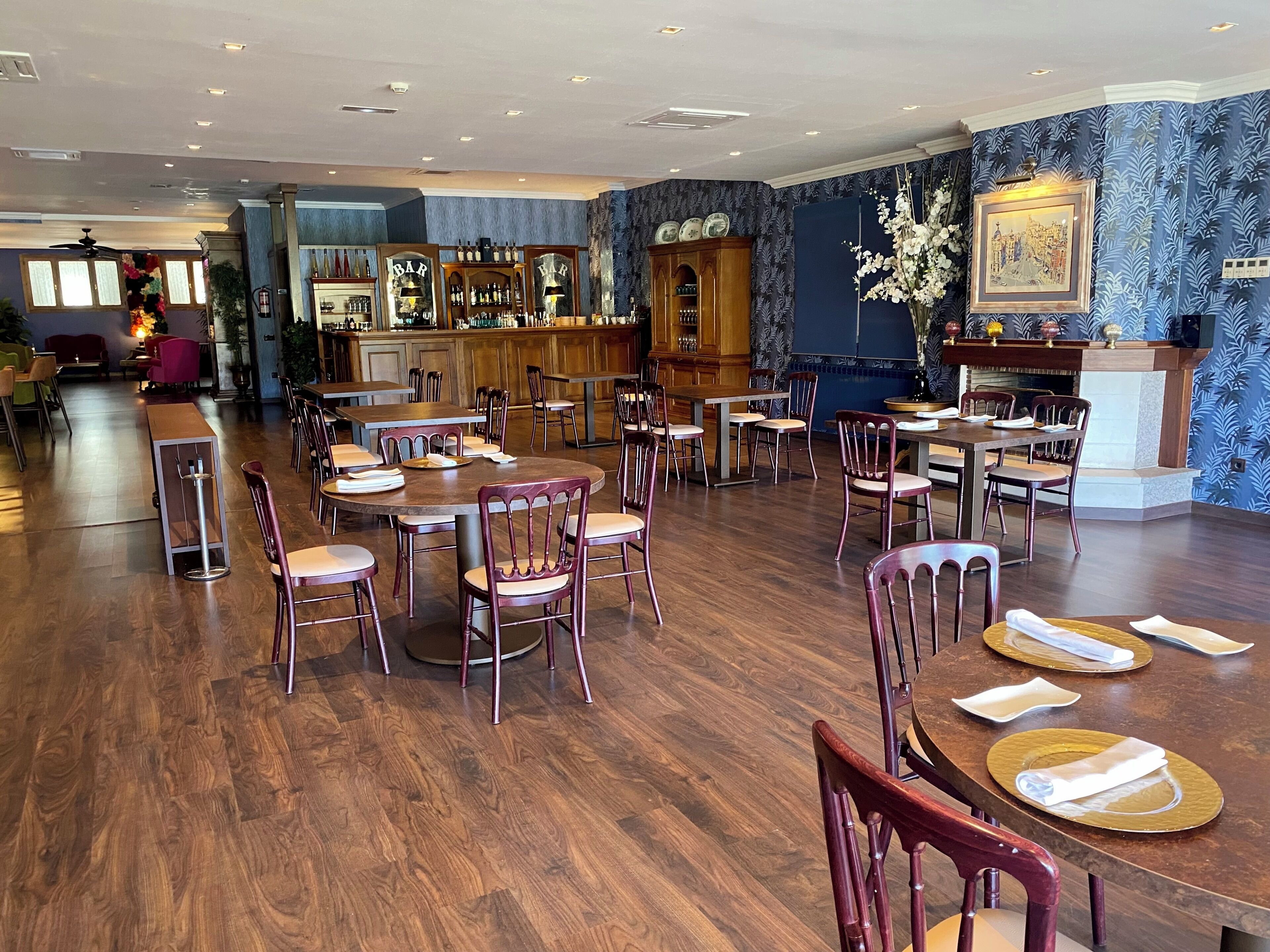 Un restaurante con mesas y sillas de madera, una zona de bar y un muro con diseño.