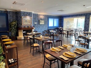 Um restaurante com várias mesas e cadeiras, lareira e obras de arte emolduradas nas paredes.