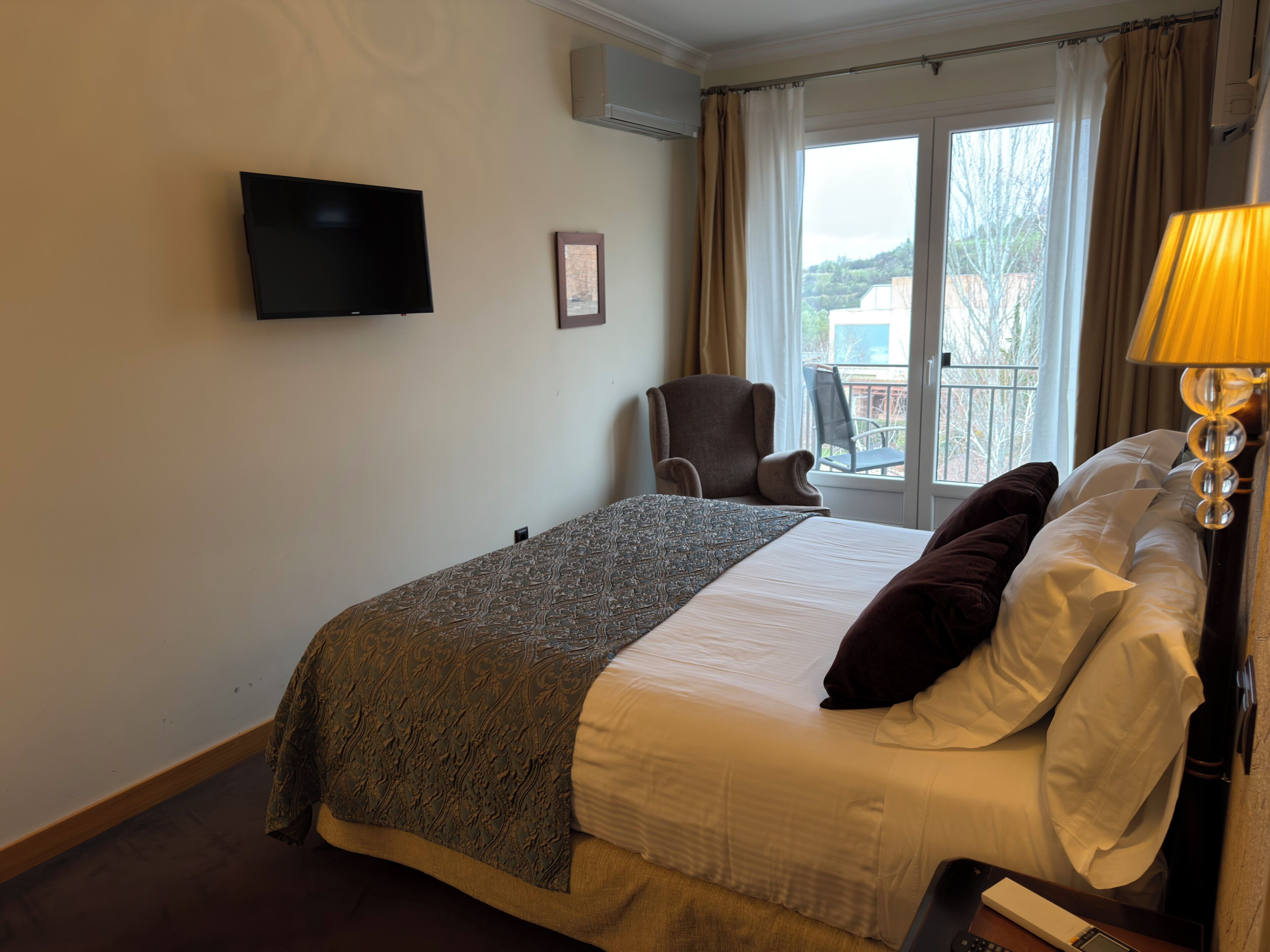 Una habitación de hotel con cama, una silla, televisión y ventana con vistas.